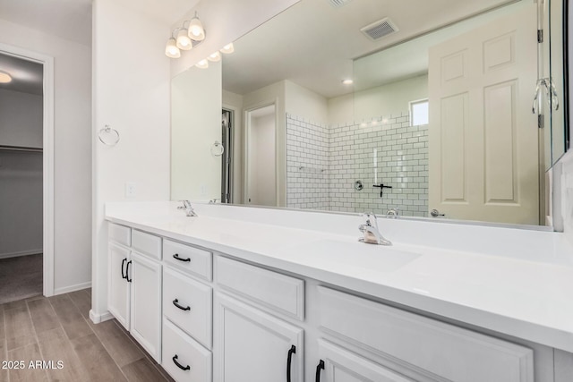 bathroom with double vanity, visible vents, a sink, wood finished floors, and tiled shower