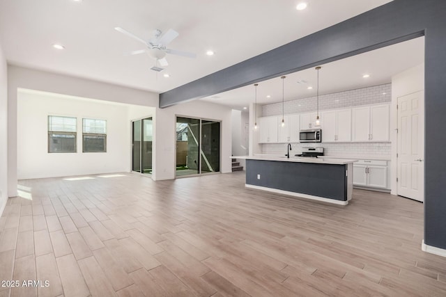 kitchen featuring light wood-style flooring, stainless steel appliances, white cabinets, open floor plan, and light countertops