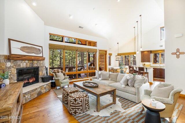 living room featuring light wood-style floors, a fireplace, visible vents, and high vaulted ceiling