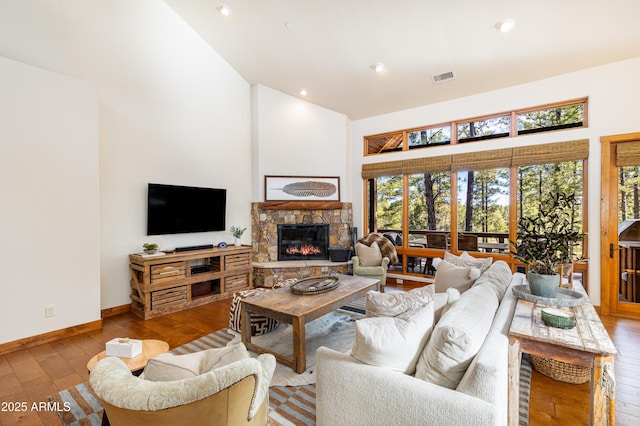 living room featuring a fireplace, wood-type flooring, visible vents, high vaulted ceiling, and baseboards