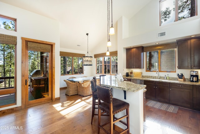 kitchen featuring dark brown cabinetry, visible vents, wood-type flooring, light stone counters, and a kitchen breakfast bar