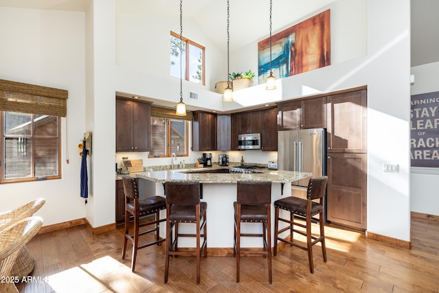 kitchen featuring a breakfast bar, dark brown cabinetry, stainless steel appliances, and light wood finished floors