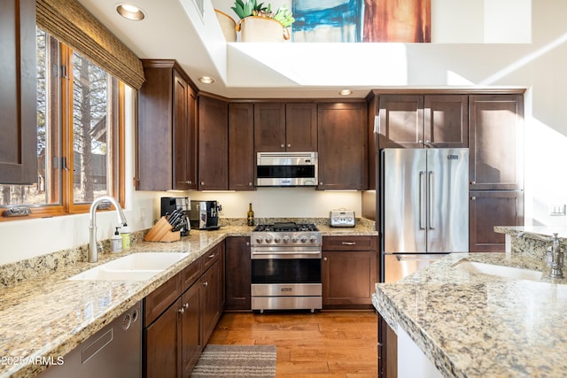 kitchen featuring light wood finished floors, premium appliances, a sink, and a healthy amount of sunlight