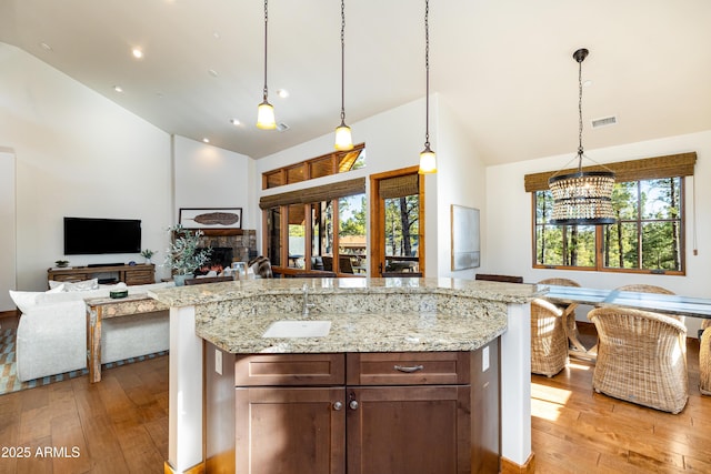 kitchen featuring open floor plan, a stone fireplace, visible vents, and light wood-style floors