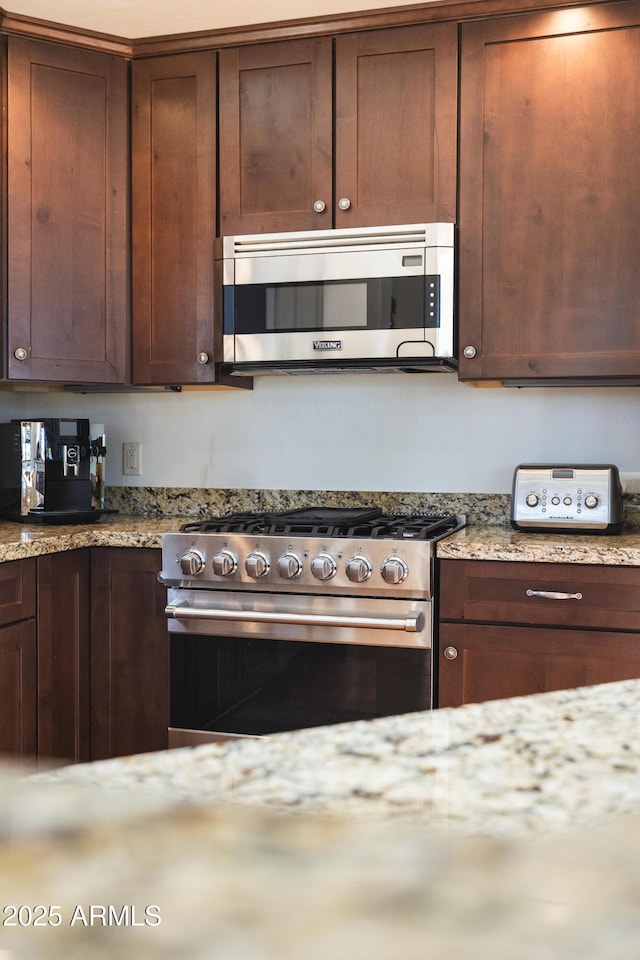 kitchen featuring appliances with stainless steel finishes, dark brown cabinetry, and light stone countertops