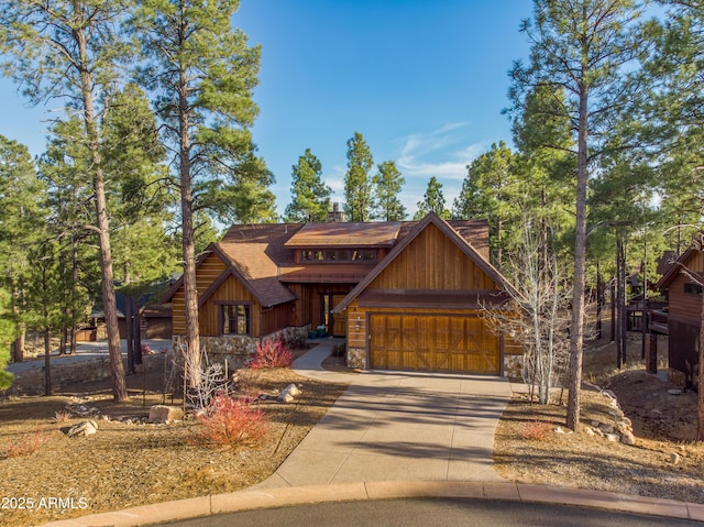 chalet / cabin with stone siding, roof with shingles, an attached garage, and concrete driveway