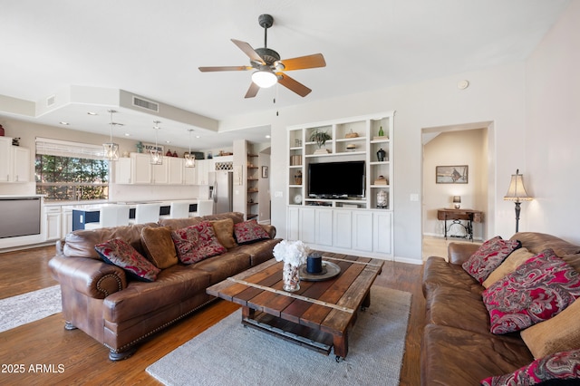 living room with ceiling fan, wood finished floors, visible vents, and built in features