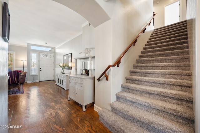 entryway featuring baseboards, arched walkways, dark wood-style floors, ornamental molding, and stairs