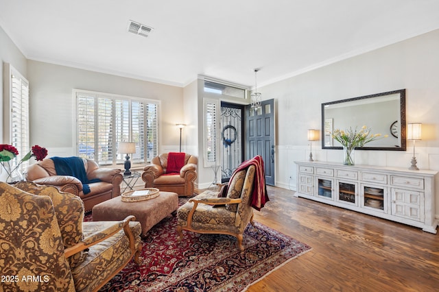 living area with a wainscoted wall, crown molding, visible vents, and wood finished floors