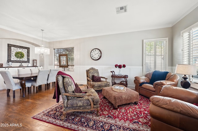 living room featuring a wainscoted wall, a notable chandelier, visible vents, ornamental molding, and wood finished floors