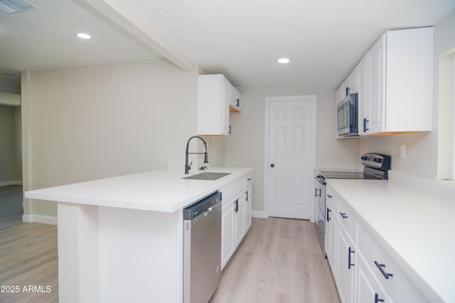 kitchen with appliances with stainless steel finishes, light wood finished floors, a sink, and visible vents