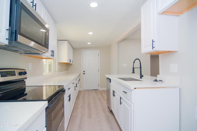 kitchen with stainless steel appliances, a sink, recessed lighting, light wood-style floors, and white cabinetry