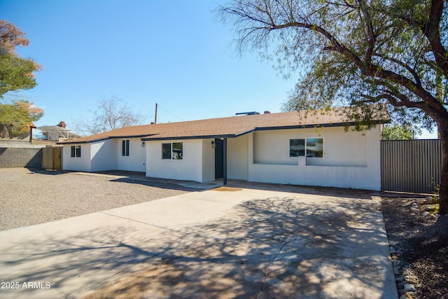 ranch-style house featuring roof with shingles, driveway, stucco siding, and fence