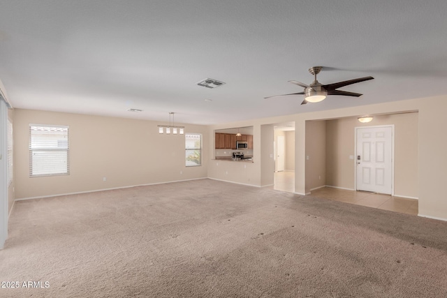 unfurnished living room featuring visible vents, light carpet, baseboards, and a ceiling fan