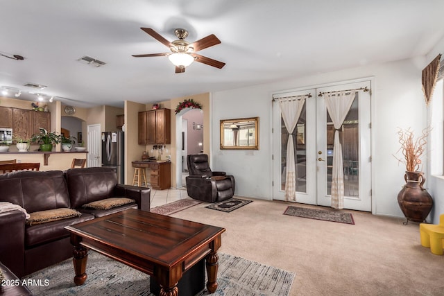 living room featuring light carpet, visible vents, arched walkways, ceiling fan, and french doors