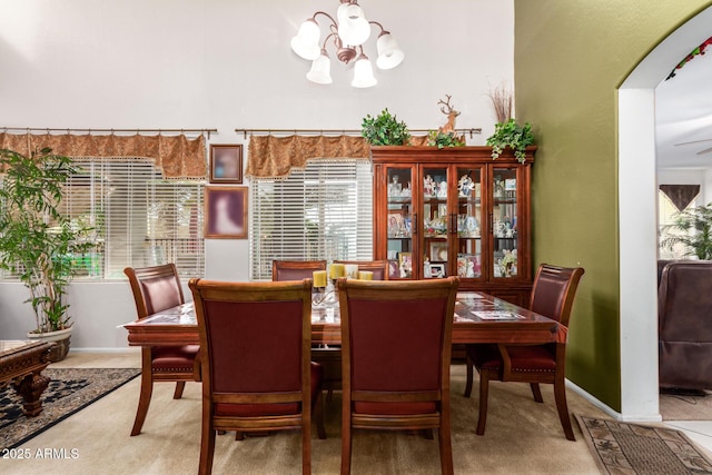 carpeted dining room featuring arched walkways, a notable chandelier, plenty of natural light, and baseboards