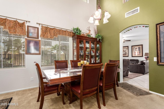 tiled dining space with visible vents, arched walkways, carpet, a high ceiling, and ceiling fan with notable chandelier