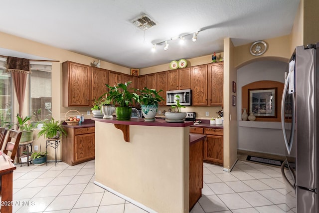 kitchen with stainless steel appliances, brown cabinetry, and light tile patterned flooring