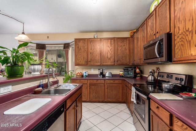 kitchen featuring stainless steel appliances, brown cabinetry, dark countertops, and a sink