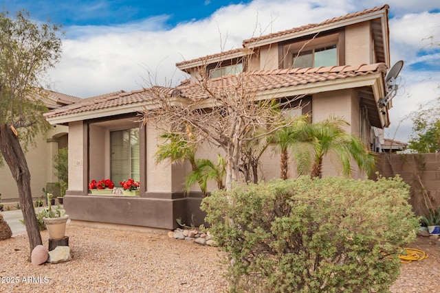 mediterranean / spanish-style home with fence, a tiled roof, and stucco siding