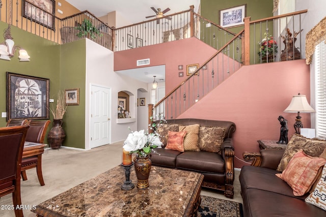 carpeted living area with arched walkways, visible vents, stairway, baseboards, and ceiling fan with notable chandelier