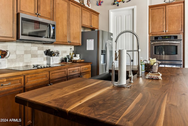 kitchen with appliances with stainless steel finishes, butcher block countertops, and decorative backsplash