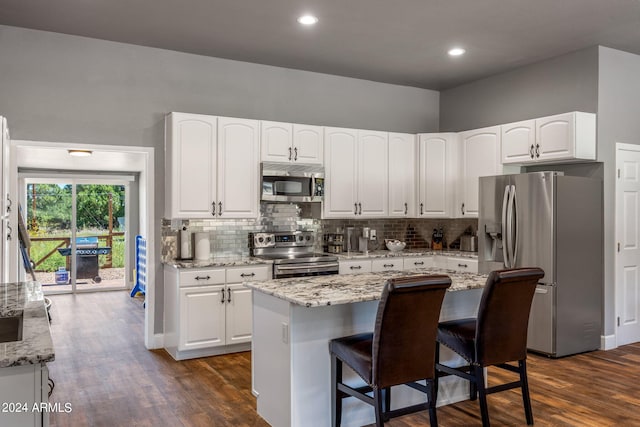 kitchen featuring dark hardwood / wood-style floors, a center island, stainless steel appliances, white cabinetry, and light stone counters