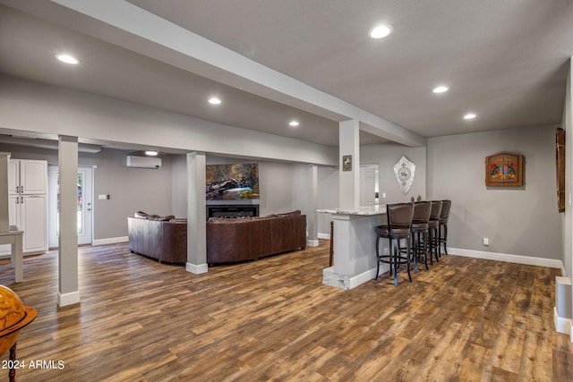 kitchen with dark wood-type flooring, a kitchen bar, light stone counters, and a wall mounted air conditioner