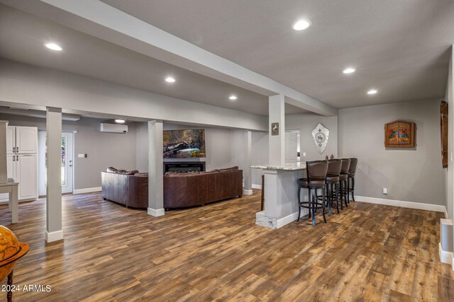 kitchen with white cabinetry, kitchen peninsula, light stone counters, dark hardwood / wood-style floors, and a breakfast bar