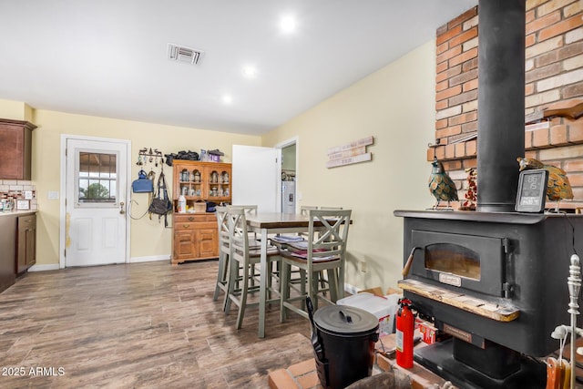 dining area with visible vents, electric water heater, wood finished floors, baseboards, and a wood stove