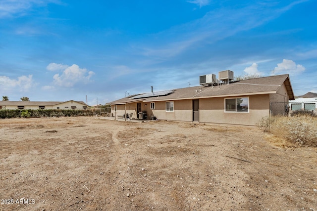 rear view of house featuring stucco siding, central air condition unit, fence, roof with shingles, and solar panels