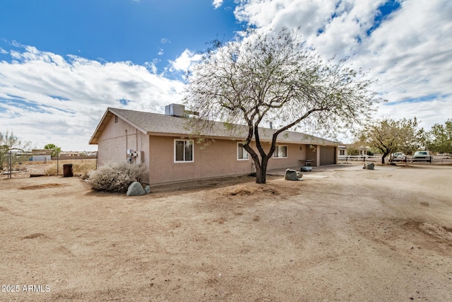 view of property exterior with cooling unit, fence, an attached garage, stucco siding, and dirt driveway