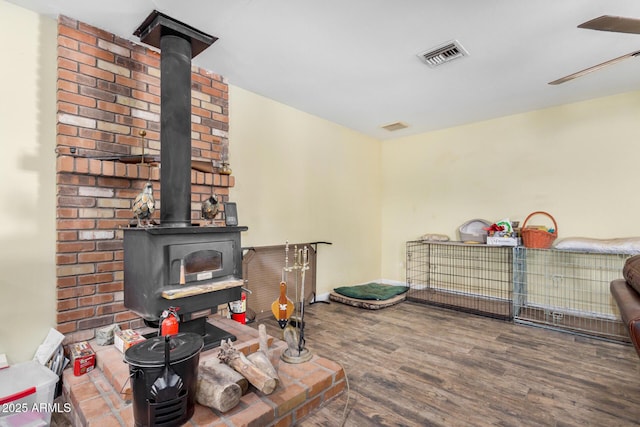 living room with visible vents, a wood stove, ceiling fan, and wood finished floors