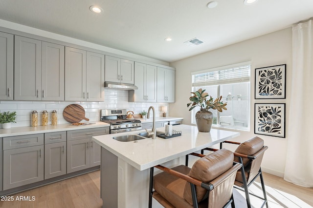 kitchen with visible vents, gray cabinetry, under cabinet range hood, a sink, and gas stove