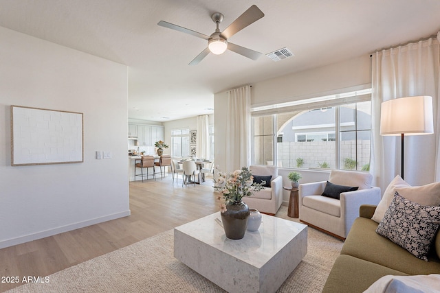 living area with visible vents, baseboards, light wood-type flooring, and ceiling fan