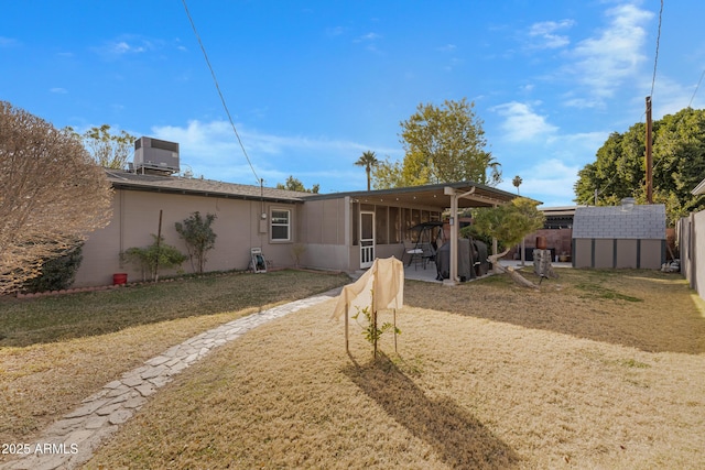 back of house featuring a sunroom, central AC unit, a lawn, and a storage shed