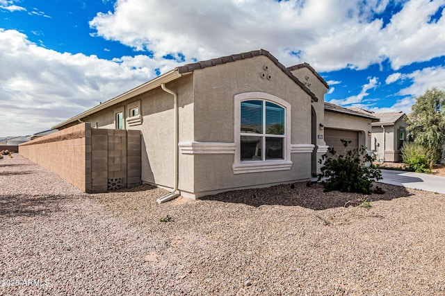 view of side of home featuring a tile roof, an attached garage, and stucco siding