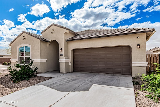 mediterranean / spanish-style home with stucco siding, driveway, fence, an attached garage, and a tiled roof