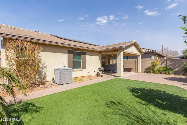 rear view of property featuring central AC unit, solar panels, a patio, a yard, and stucco siding