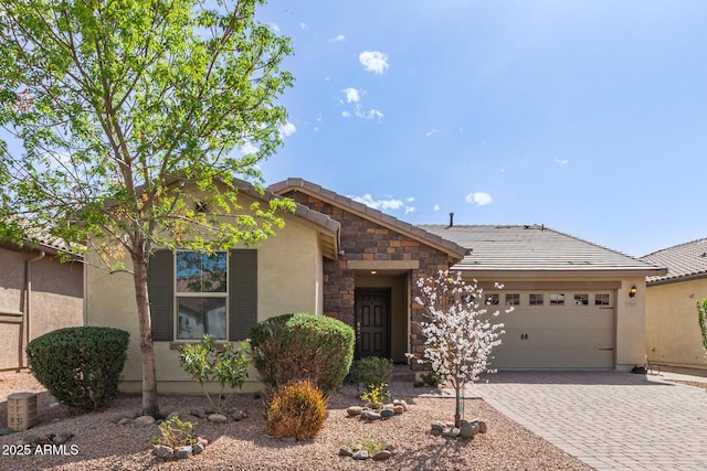 view of front facade with an attached garage, a tile roof, stone siding, decorative driveway, and stucco siding