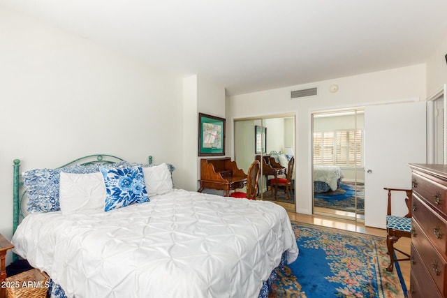 bedroom featuring two closets, visible vents, and wood finished floors