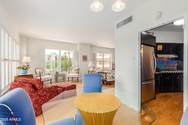 living area featuring light wood-type flooring, visible vents, and a notable chandelier