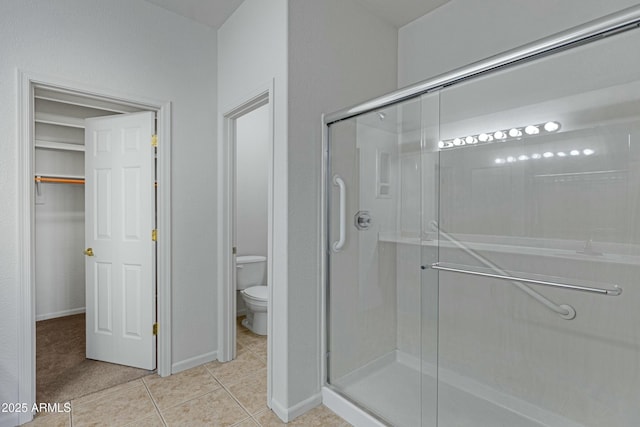 bathroom featuring a stall shower, baseboards, tile patterned flooring, and toilet