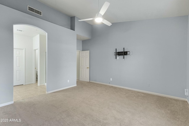 spare room featuring light carpet, visible vents, arched walkways, ceiling fan, and high vaulted ceiling