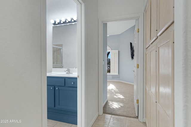 hall featuring light tile patterned floors, a sink, light colored carpet, and baseboards