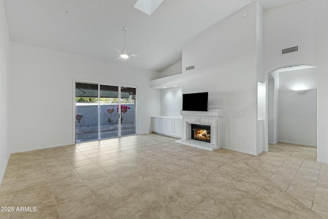 unfurnished living room featuring a warm lit fireplace, a skylight, visible vents, arched walkways, and ceiling fan