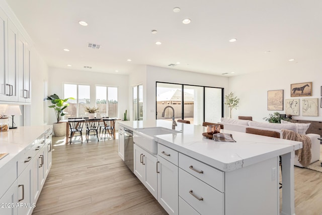 kitchen featuring dishwasher, sink, white cabinets, light stone counters, and a center island with sink