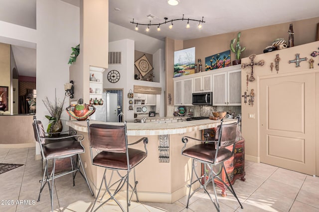 kitchen with light tile patterned flooring, lofted ceiling, a breakfast bar area, tile countertops, and kitchen peninsula