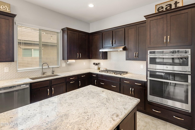 kitchen with stainless steel appliances, backsplash, a sink, dark brown cabinetry, and under cabinet range hood