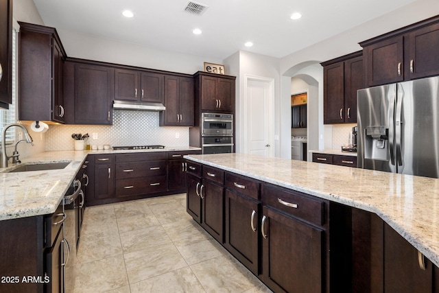 kitchen featuring light stone counters, visible vents, appliances with stainless steel finishes, a sink, and under cabinet range hood